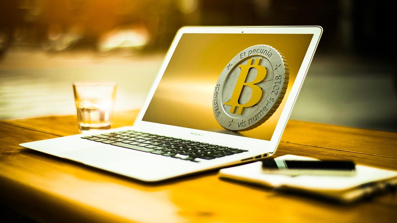 bitcoin on the screen of a laptop, glass, notepad and pen on a table